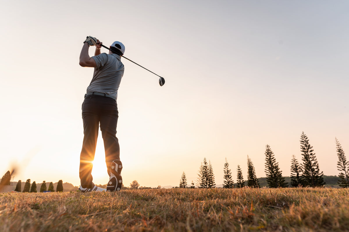 Golfer im Ausschwung mit einem Driver auf dem Golfplatz im Abendlicht